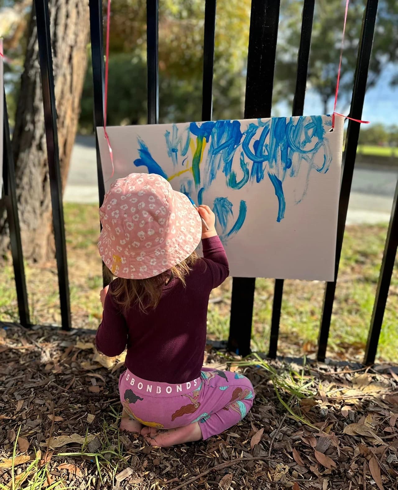 Child painting on a black canvas outdoors during a creative learning-through-play activity.