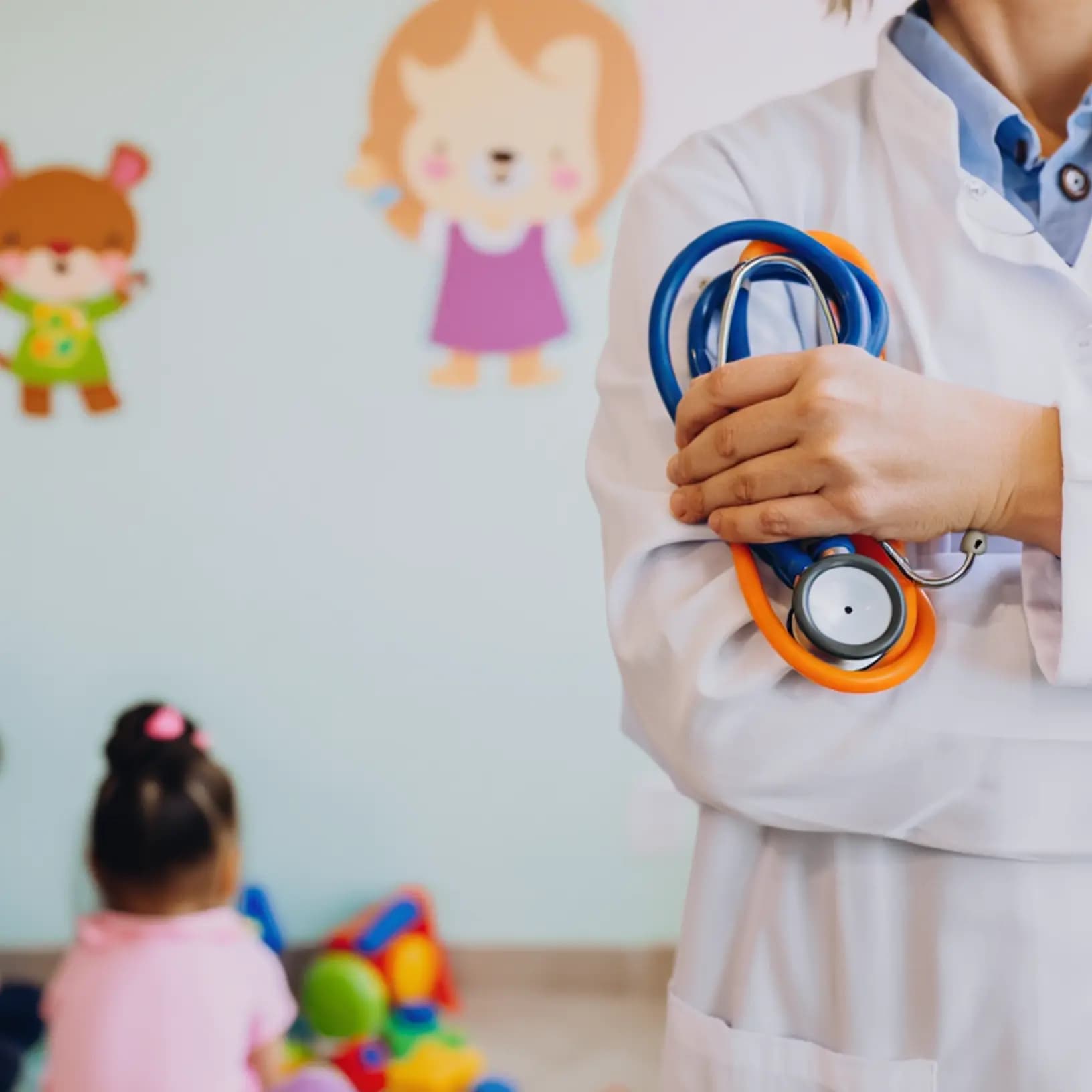 Doctor holding a stethoscope while children play safely in the background during the service’s routine wellness check.