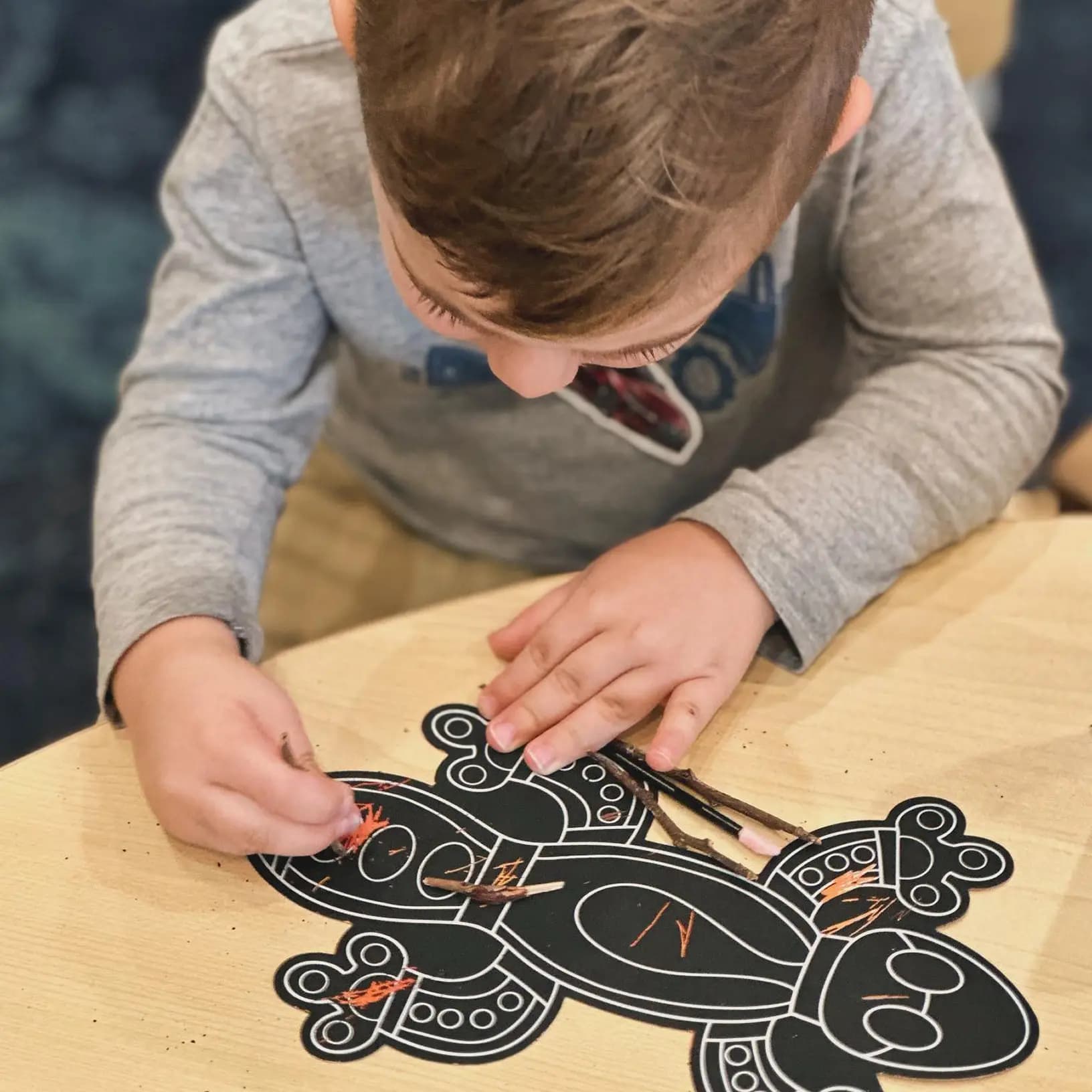 Child decorating an animal-shaped craft using sticks and crayons as part of a play-based early learning activity.