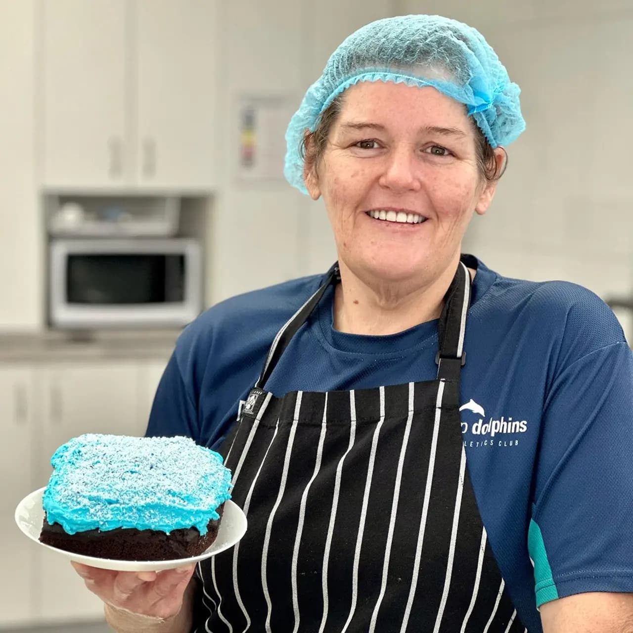 Moolanda’s chef proudly holding a homemade blue-frosted cake, supporting healthy meal services for children.